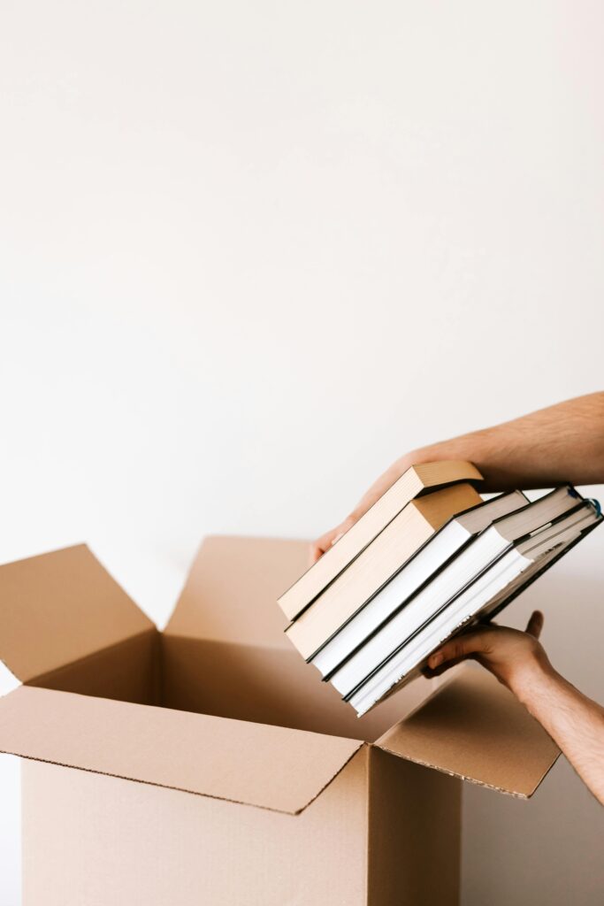 pexels-photo-4498137-4498137 Person organizing and packing books into a cardboard box, preparing for relocation.