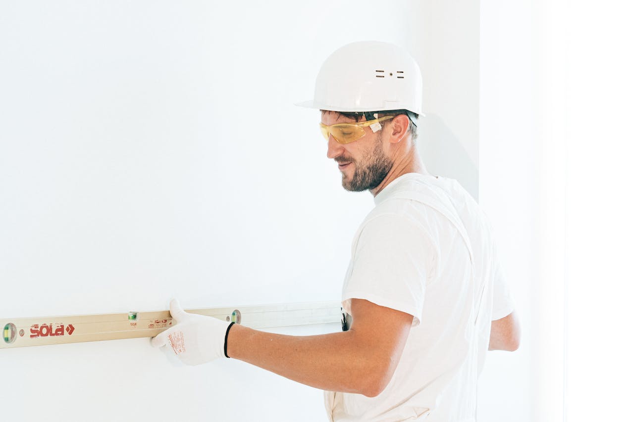 Man wearing safety gear using a spirit level indoors for construction work.