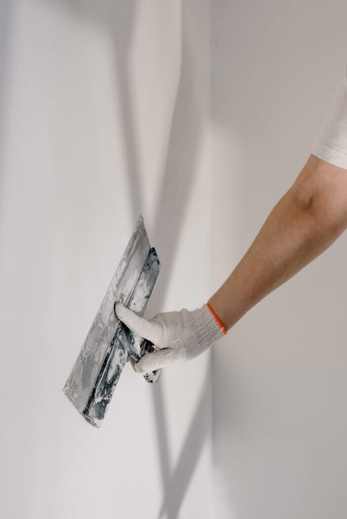 pexels-photo-5691622 Crop anonymous male worker in gloves holding putty knife while working at home