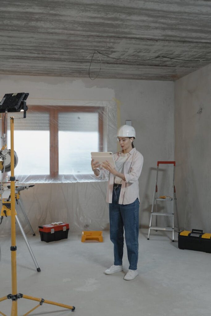 pexels-photo-6474476 Woman in construction helmet reviewing plans on a tablet at an indoor renovation site.
